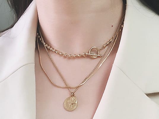 goldene Layering-Halskette mit Münzanhängern und Kugelketten auf einem Model
